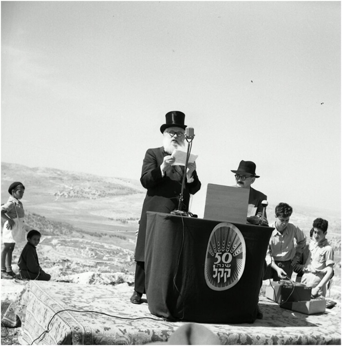 הרב הראשי הרצוג נואם בעת טקס חנוכת יער הקדושים מעל דוכן עם סמל החגיגות היובל לקק"ל. באדיבות הארכיון הציוני המרכזי NSC\103959. צלם: לא ידוע